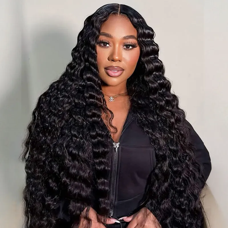 Portrait of a woman with long, wavy black hair wearing a black zip-up jacket and gold necklace in front of a light background.