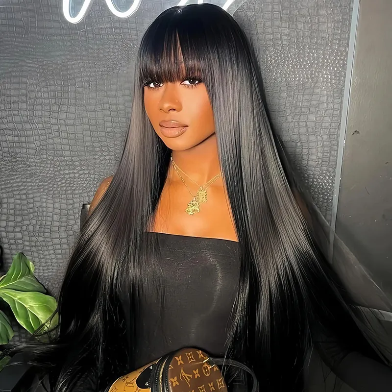 Woman with long, sleek black hair and blunt bangs posing against a textured wall in a black strapless top, wearing gold necklaces.