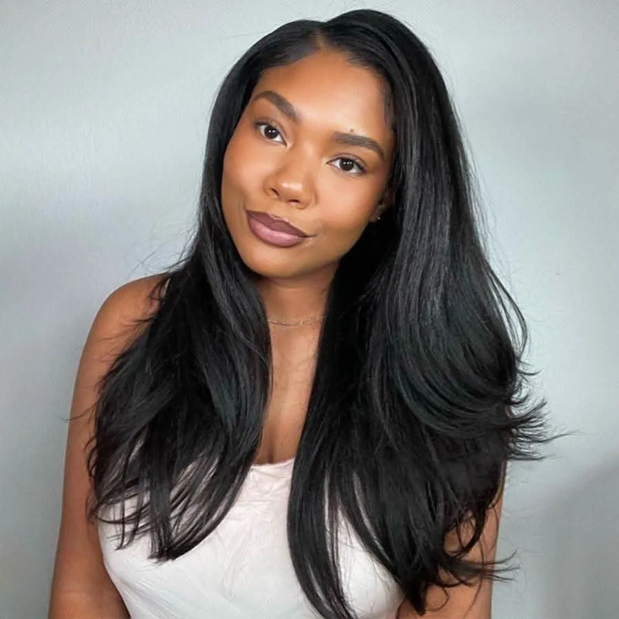 Portrait of a woman with long, straight black hair and subtle makeup, wearing a white top against a light gray background, looking at the camera.